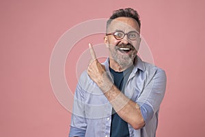 Excited man in blue shirt, pointing upwards with finger, having great idea, isolated on pink background
