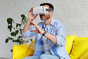 Excited man in blue shirt wearing virtual reality glasses touching something and smiling while having VR experience