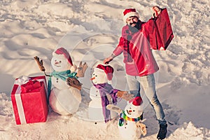 Excited man with funny snowman in stylish hat and scarf on snowy field. Happy winter snowman family with gift. Mother