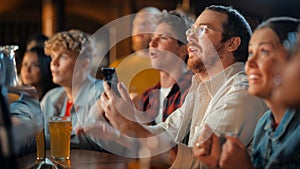 Excited Man in Glasses Sitting at a Bar Stand, Using a Smartphone, Feeling Alive After Putting a Bet