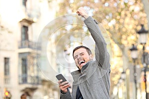 Excited man holding phone and raising arm in the street