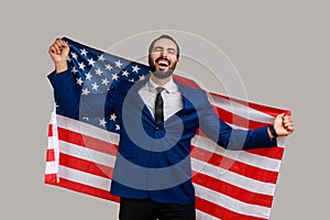 Excited man holding USA flag and looking at camera with rejoice look, celebrating national holiday.