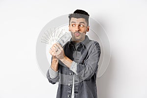 Excited man hugging and kissing dollar bills, holding money and rejoicing, standing on white background