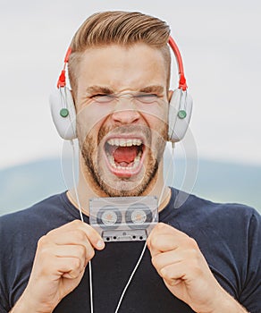 Excited Man listening music in headphones with cassette. Emotional screaming portrait guy. Young bearded good-looking