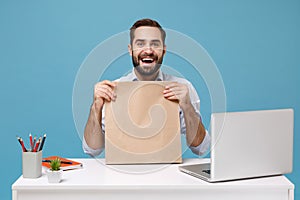 Excited man in shirt sit work at desk with pc laptop isolated on blue background. Food products delivery courier service