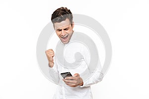 Excited man with short dark hair holding smartphone and clenching fist, isolated over white background