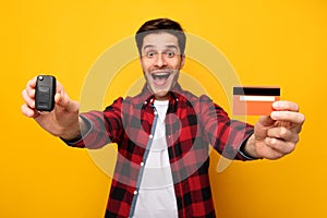 Excited Man Showing Car Key And Credit Card, Yellow Background