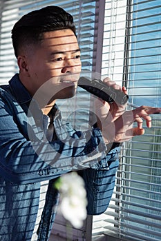 excited man spying through window blinds with binoculars