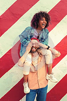 Excited man standing against the wall and carrying girlfriend on his shoulders