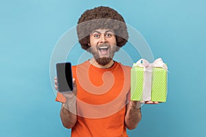 Excited man standing with present box and showing cell phone with empty display.