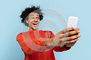 Excited man taking selfie with smartphone on blue background