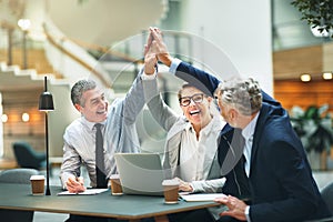 Excited mature businesspeople high fiving together in a modern o