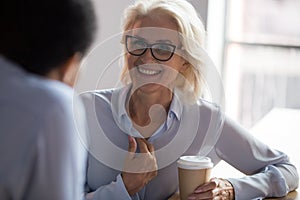 Excited mature businesswoman talking with colleague during coffee break