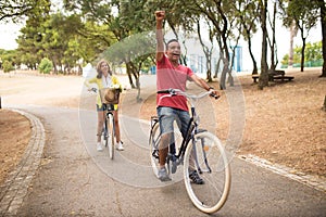 Excited mature couple riding bicycles in park