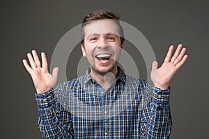 Excited mature man standing with raised hands and looking at camera.