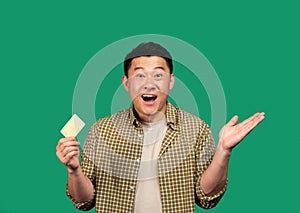 Excited middle aged asian man holding credit card, raising hands up rejoicing to success isolated on green background