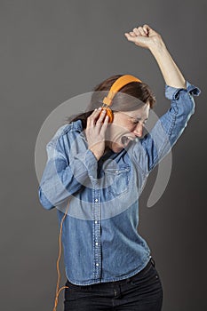 Excited middle aged woman enjoying shouting, listening to funky music