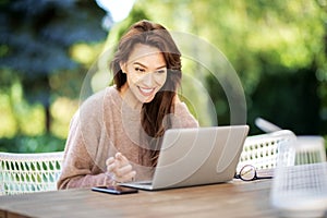 Excited middle aged woman using a laptop while sitting on balcony at home