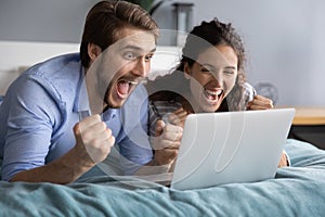 Excited millennial couple celebrate online win on laptop