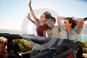 Excited millennial friends travelling in the back of an open car with their arms in the air photo