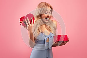 Excited millennial lady getting Valentine& x27;s Day surprise, opening heart shaped gift box on pink studio background