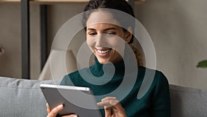 Excited millennial latina female using modern electronic tablet at home