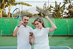 excited mixed doubles athletes using cell phones together