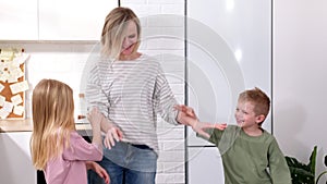 Excited mom or babysiter and two kids boy and girl jumping dancing laughing in modern scandinavian house kitchen Happy