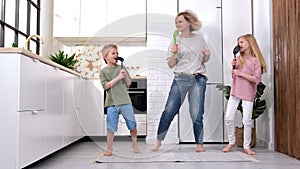Excited mom or babysiter and two kids boy and girl jumping dancing laughing in modern scandinavian house kitchen Happy