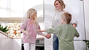 Excited mom or babysiter and two kids boy and girl jumping dancing laughing in modern scandinavian house kitchen Happy