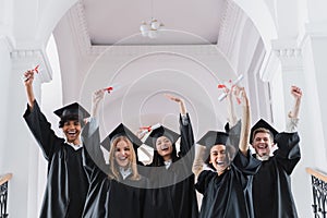 Excited multicultural students with diplomas showing