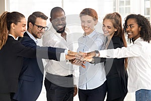 Excited multiethnic employees stack hands showing support and unity