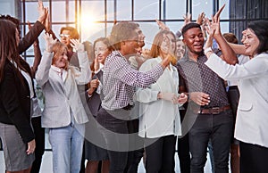 Excited multinational employees celebrating team victory giving high five gathered in office,
