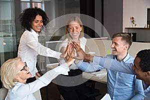 Excited diverse colleagues join hands showing unity at meeting