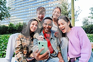 Excited multiracial group of friends enjoying and smiling using a cellphone app. Diverse teenagers having fun watching
