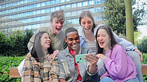 Excited multiracial group of friends enjoying and smiling using a cellphone app. Diverse teenagers having fun watching