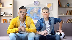 Excited multiracial teen fans watching football match at home, leisure activity
