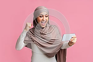 Excited Muslim Woman In Hijab Celebrating Success With Smartphone In Hands