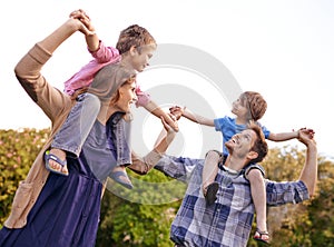 Excited, nature and children on parents shoulders in outdoor park or field for playing together. Happy, bonding and