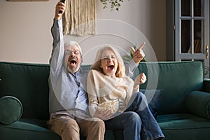 Excited old couple holding remote control watching tv celebrate victory