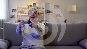 Excited old woman playing video game on joystick, rejoicing victory, entertain