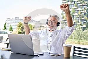 Excited older business man looking at laptop raising fists winning online.