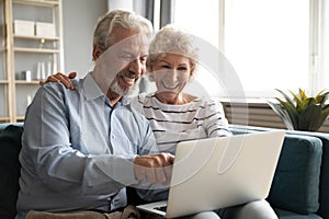 Excited older couple reading good news, using laptop together
