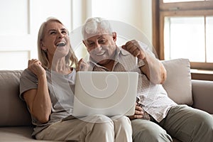 Excited older wife and husband celebrating online win, using laptop