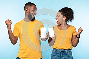 Excited over this new mobile app. Overjoyed black couple holding smartphones with mockup for design, making YES gestures