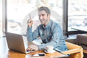 Excited overjoyed man working on laptop and raised finger up, having good idea, discussing project.