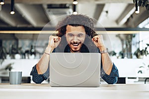 Excited overjoyed young businessman looking at laptop screen happy to win or recieved good news