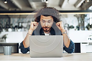 Excited overjoyed young businessman looking at laptop screen happy to win or recieved good news