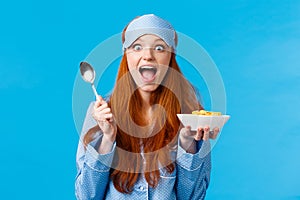 Excited, overwhelmed happy redhead caucasian woman eating cereals morning, holding spoon, smiling amused and amazed