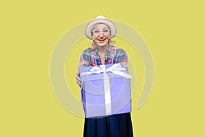 Excited positive mature woman in shirt and eyeglasses giving present box congratulating with holiday